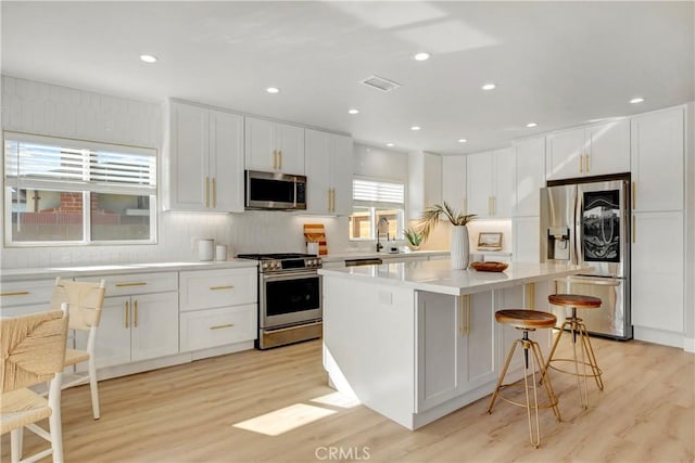 kitchen featuring appliances with stainless steel finishes, white cabinetry, sink, a kitchen bar, and a center island