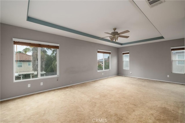 empty room with ceiling fan, a tray ceiling, and light carpet