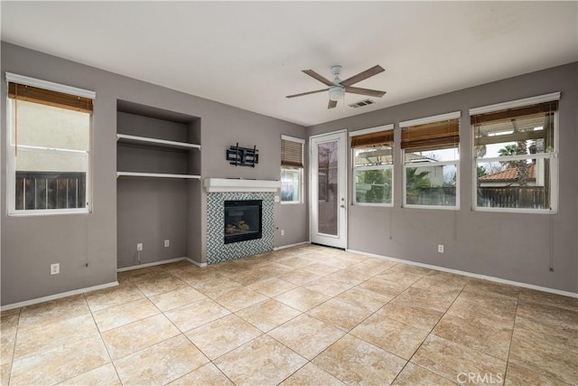 unfurnished living room with a tiled fireplace, light tile patterned floors, ceiling fan, and built in shelves