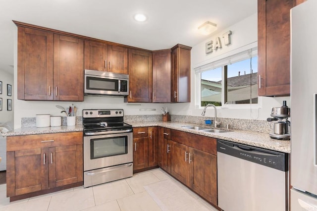 kitchen featuring appliances with stainless steel finishes, light stone countertops, sink, and light tile patterned floors