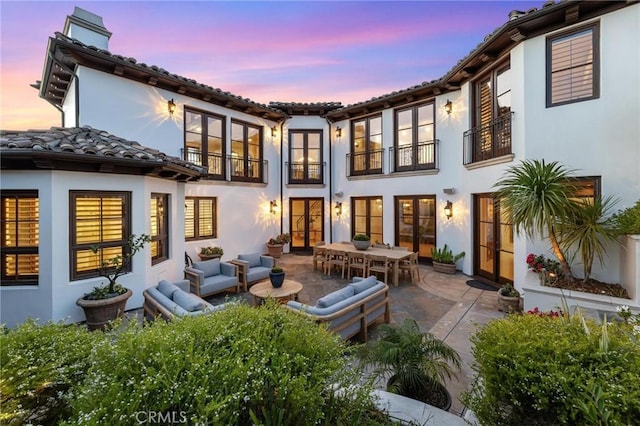 back house at dusk with an outdoor living space, a patio area, and french doors