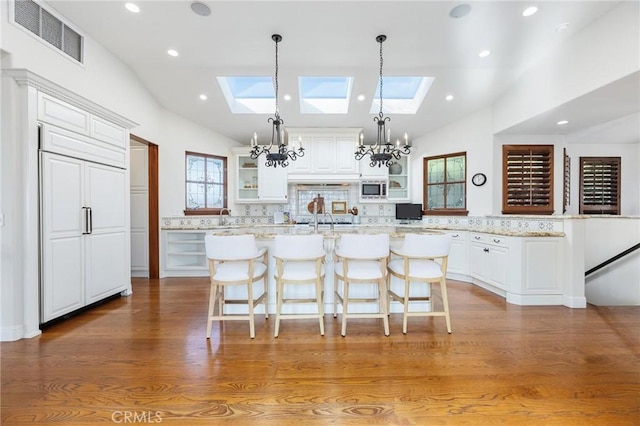 212 John St, Manhattan Beach, CA 90266 - kitchen featuring an inviting chandelier, glass insert cabinets, visible vents, a kitchen island with sink, and built in appliances
