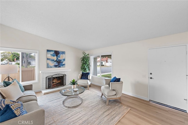 living room with vaulted ceiling, a textured ceiling, a fireplace, and light hardwood / wood-style flooring