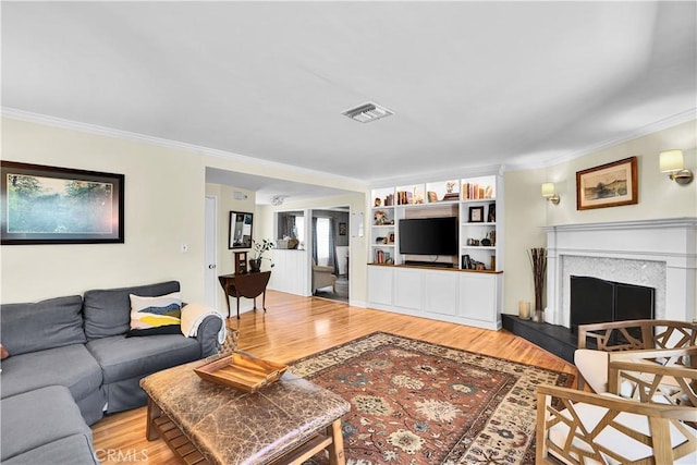 living room with light wood-type flooring, visible vents, a fireplace with raised hearth, and crown molding