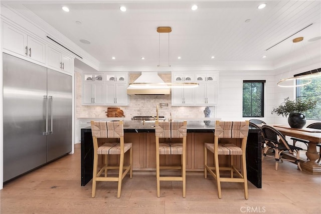 kitchen featuring stainless steel built in fridge, glass insert cabinets, and a large island with sink