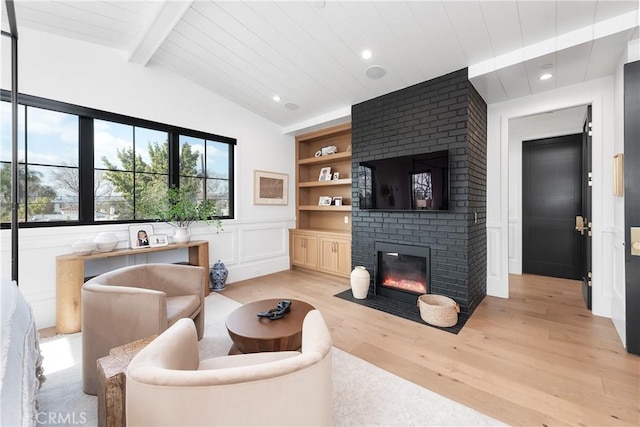 living area featuring lofted ceiling with beams, built in shelves, a decorative wall, a fireplace, and light wood-style floors