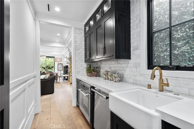 kitchen featuring light countertops, a sink, light wood-style flooring, and dark cabinetry