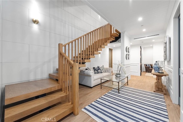 living room featuring light wood-type flooring, a decorative wall, and stairway