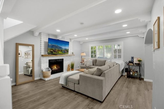 living room with beamed ceiling, a brick fireplace, and hardwood / wood-style flooring