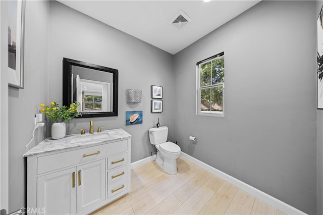 half bath with baseboards, visible vents, toilet, wood finished floors, and vanity