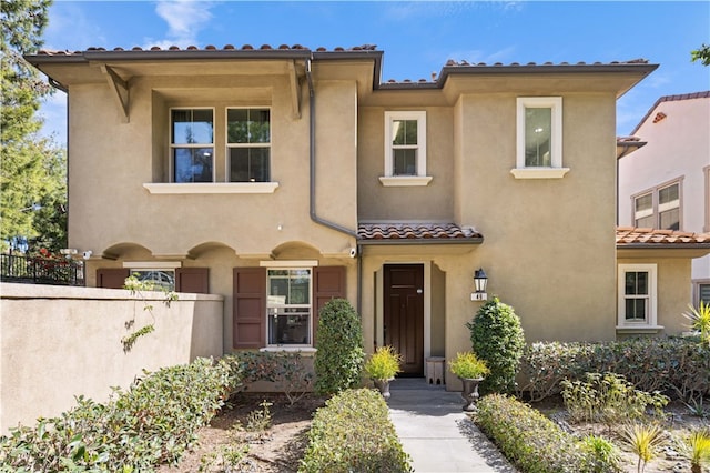 mediterranean / spanish-style house with a tile roof, fence, and stucco siding