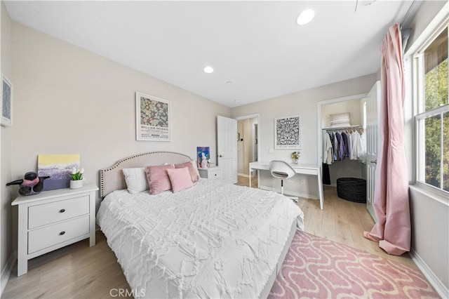 bedroom with baseboards, light wood-style flooring, a walk in closet, a closet, and recessed lighting