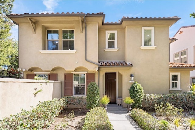 mediterranean / spanish home with a tiled roof, stucco siding, and fence