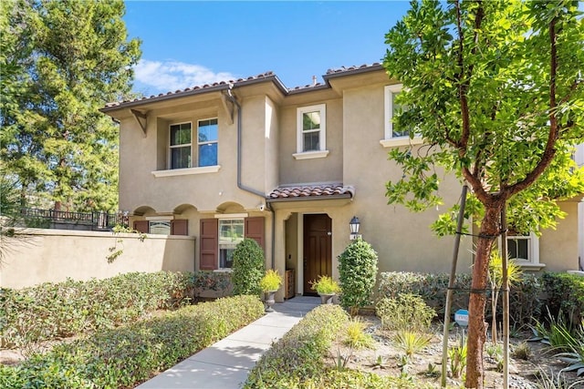 mediterranean / spanish-style home featuring a tile roof, fence, and stucco siding