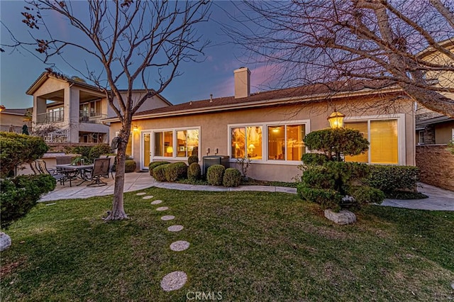 back house at dusk with a patio area and a lawn