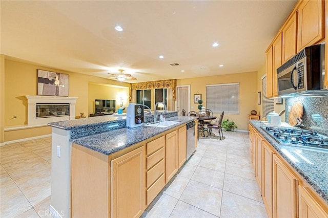 kitchen with light brown cabinetry, sink, dark stone counters, a kitchen island with sink, and stainless steel appliances