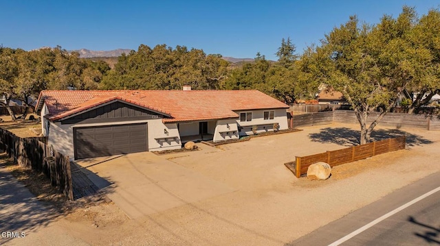 view of front of home featuring driveway, a tiled roof, an attached garage, fence, and board and batten siding