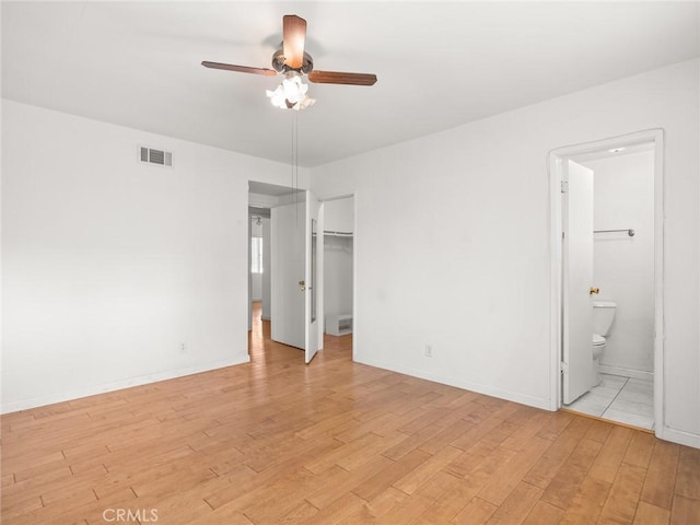 unfurnished bedroom with a walk in closet, ensuite bath, a closet, ceiling fan, and light hardwood / wood-style floors