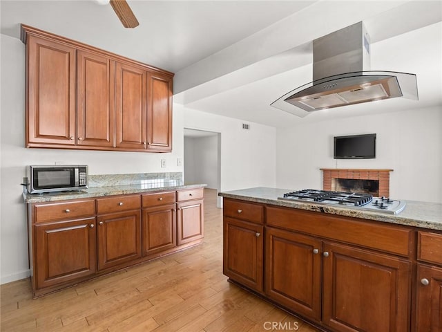 kitchen featuring island range hood, ceiling fan, light stone counters, stainless steel appliances, and light hardwood / wood-style floors