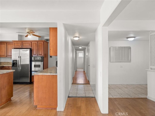 kitchen featuring light stone countertops, stainless steel appliances, ceiling fan, and light wood-type flooring