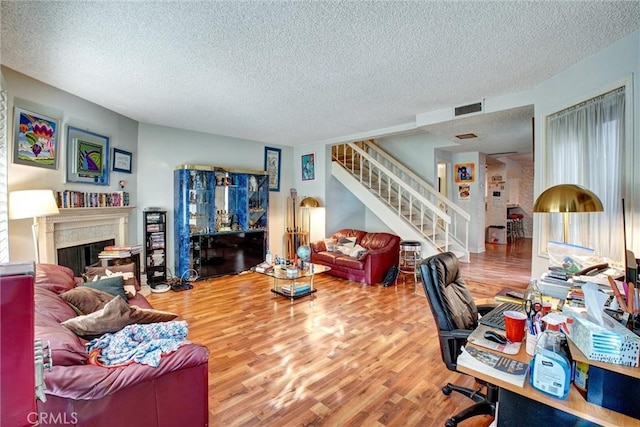 living area with visible vents, a high end fireplace, a textured ceiling, wood finished floors, and stairs