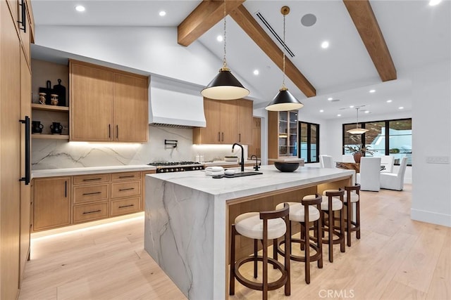 kitchen featuring hanging light fixtures, a large island with sink, light stone countertops, custom range hood, and beam ceiling