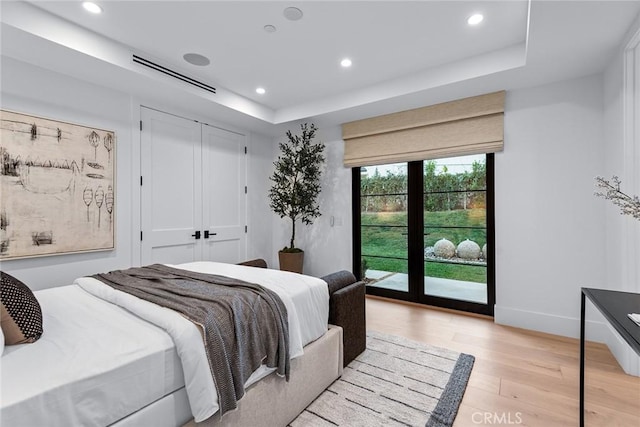 bedroom featuring a raised ceiling, a closet, access to exterior, and light hardwood / wood-style flooring