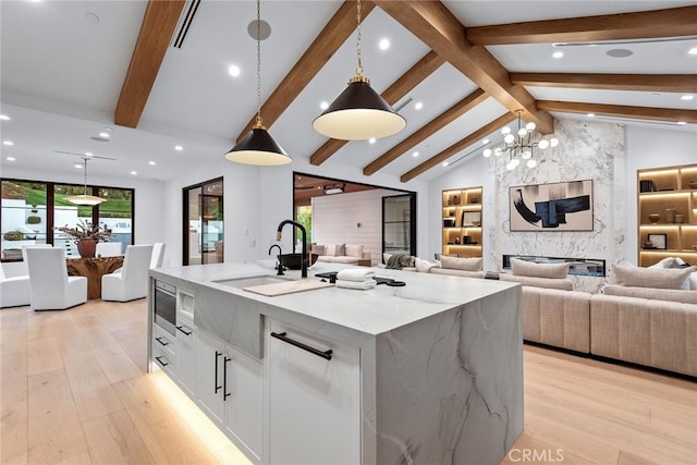 kitchen featuring sink, white cabinetry, hanging light fixtures, a large island, and light stone countertops