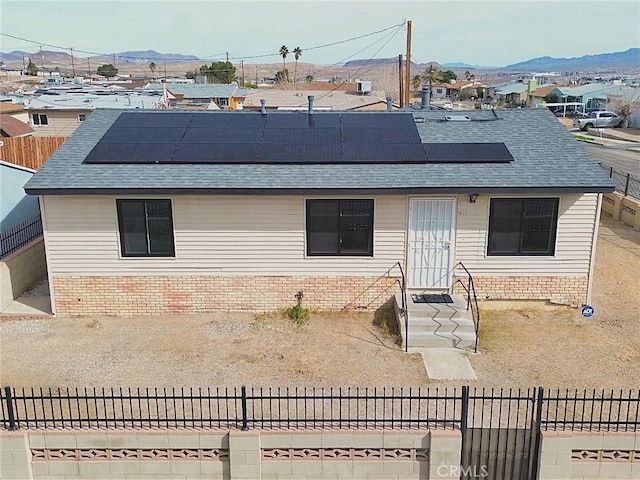 view of front facade with brick siding, a shingled roof, a mountain view, and roof mounted solar panels