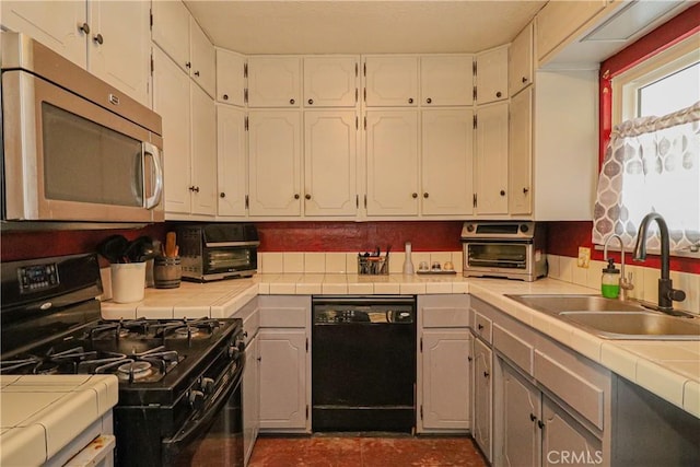 kitchen with a toaster, a sink, white cabinetry, tile counters, and black appliances