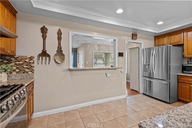 kitchen with ornamental molding, appliances with stainless steel finishes, light stone counters, and a tray ceiling