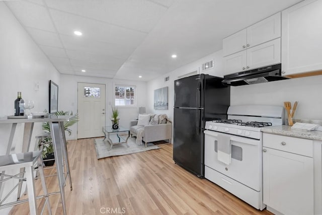 kitchen featuring black refrigerator, white cabinetry, white range with gas stovetop, light hardwood / wood-style floors, and light stone countertops