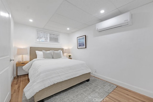 bedroom featuring wood-type flooring, a wall mounted AC, and a drop ceiling