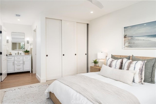 bedroom with connected bathroom, sink, light hardwood / wood-style floors, and a closet