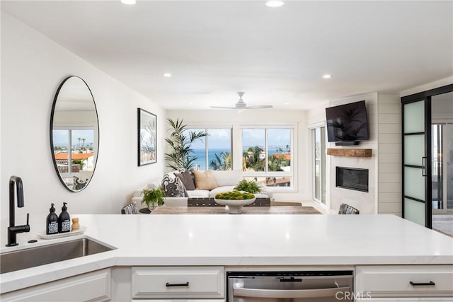 kitchen featuring white cabinetry, sink, a large fireplace, stainless steel dishwasher, and ceiling fan