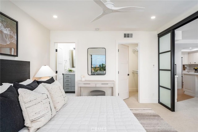 bedroom with light carpet, a spacious closet, ensuite bath, and ceiling fan