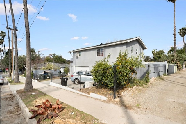 view of side of property featuring stucco siding, a garage, and fence