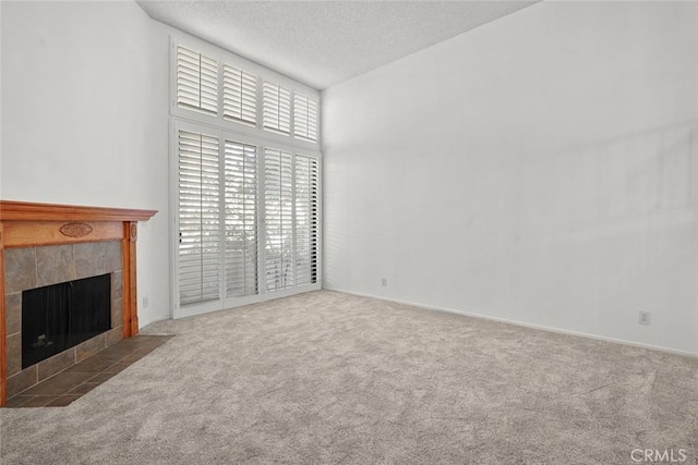 unfurnished living room featuring carpet floors, a tile fireplace, a textured ceiling, and a high ceiling