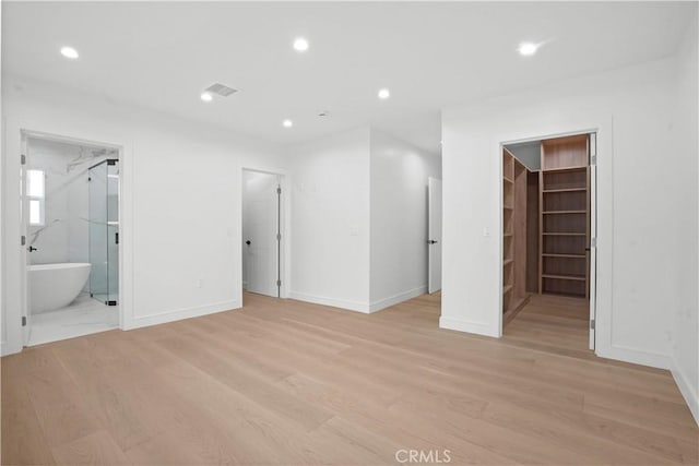 unfurnished bedroom featuring ensuite bath, a walk in closet, a closet, and light wood-type flooring