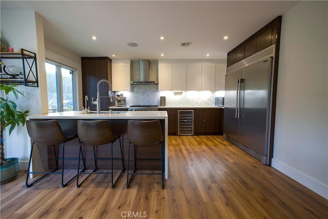 kitchen featuring light countertops, visible vents, appliances with stainless steel finishes, beverage cooler, and wall chimney exhaust hood