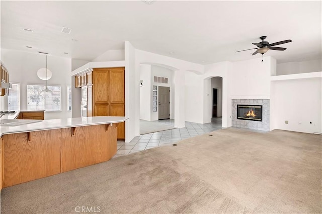 kitchen featuring hanging light fixtures, a kitchen bar, a tiled fireplace, light colored carpet, and kitchen peninsula