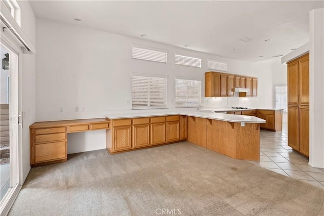 kitchen with a breakfast bar area, black gas cooktop, built in desk, light carpet, and kitchen peninsula