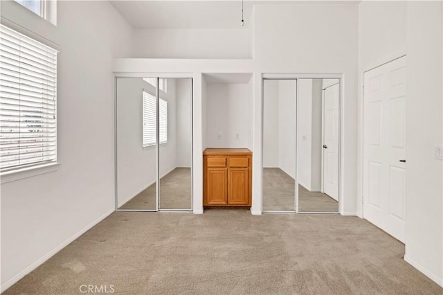 unfurnished bedroom featuring multiple windows, light carpet, and two closets