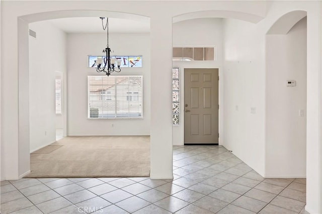 entryway with light colored carpet, a towering ceiling, and a notable chandelier