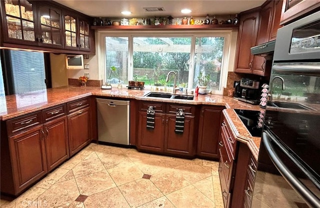 kitchen with sink, double oven, light stone counters, decorative backsplash, and stainless steel dishwasher