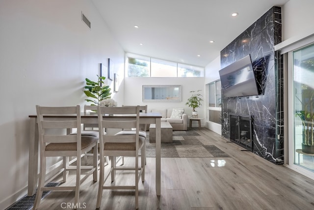 dining space featuring wood-type flooring, high vaulted ceiling, a healthy amount of sunlight, and a fireplace