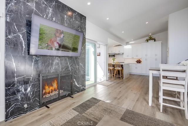 living room with vaulted ceiling, a high end fireplace, and light hardwood / wood-style floors