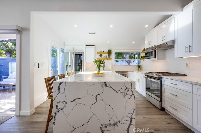 kitchen with a wealth of natural light, white cabinets, a center island, stainless steel appliances, and light stone countertops