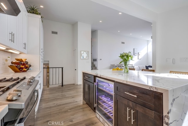 kitchen with extractor fan, white cabinetry, wine cooler, light stone counters, and dark brown cabinets