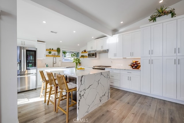 kitchen featuring a kitchen island, appliances with stainless steel finishes, lofted ceiling with beams, white cabinetry, and light stone countertops